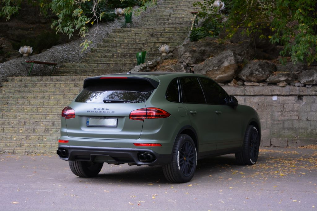 A green porsche cayen parked in front of a stone wall